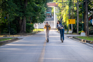Two women riding scooters down a street