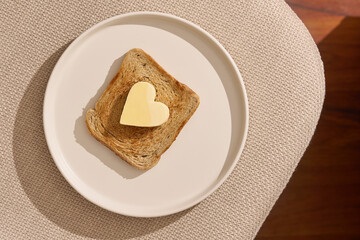 Tasty toasted bread with heart shaped butter on white modern plate with beautiful morning light. Studiio shot, minimal breakfast concept.                               