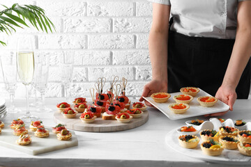 Woman with many different tasty canapes at white wooden table, closeup