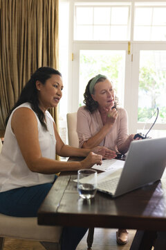 Senior women collaborating on laptop at home, discussing project with focus