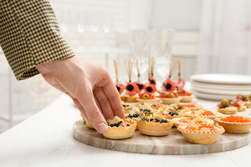 Woman taking tasty canape at white wooden table, closeup