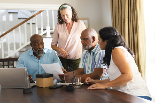Senior friends discussing documents at home, collaborating around table with laptop