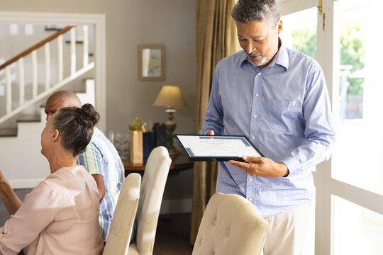 Senior man proudly holding award certificate at family gathering in dining room