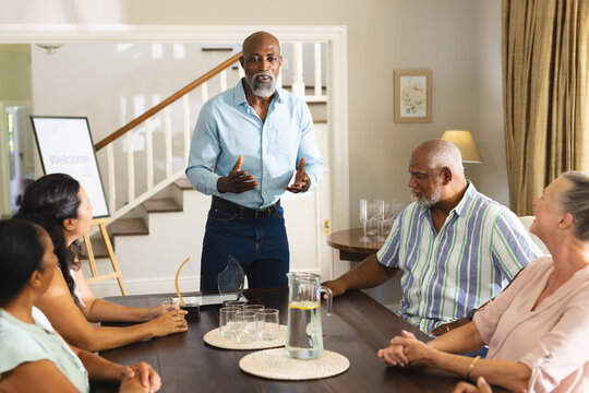 Giving speech, senior man at family gathering, everyone at dining table listening