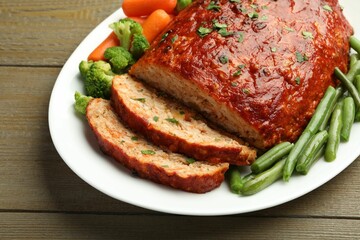 Delicious baked turkey meatloaf with vegetables on wooden table, closeup