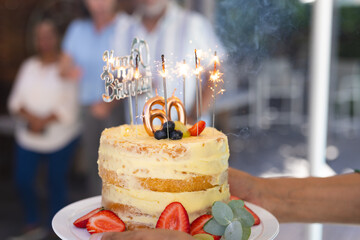 Celebrating 60th birthday with sparklers on cake, surrounded by diverse senior friends and diverse s