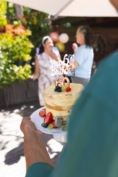 Celebrating 60th birthday outdoors with cake and joyful diverse senior friends in garden
