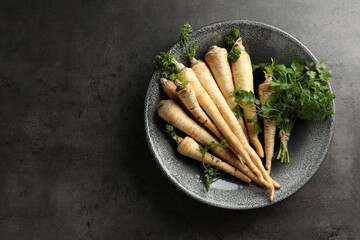 Parsley roots with leaves on black table, top view. Space for text