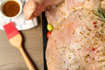 Whole raw turkey with marinade and basting brush on wooden table, above view