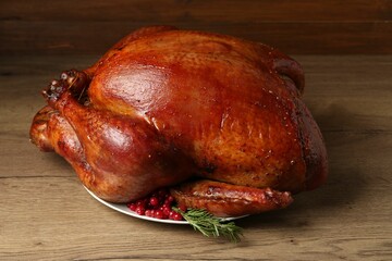 Whole baked turkey with cranberries and rosemary on wooden table, closeup