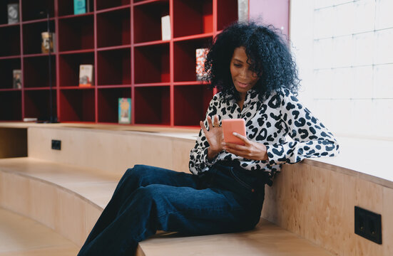 Smiling woman using smartphone to send money securely via banking app.Sitting in modern coworking space,she enjoys convenience of instant online transactions,ensuring fast and reliable payment process