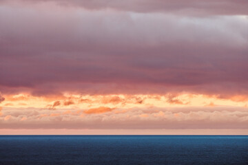 A stunning ocean view at sunset with vibrant orange and pink clouds contrasting against the calm blue water and dramatic sky