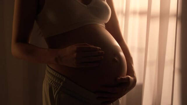 Young happy pregnant woman posing in studio with white curtains in background