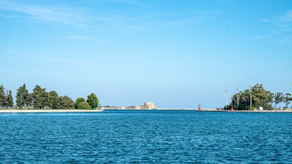 Serene waterfront cityscape with greenery and blue sky.