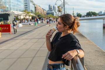 Fototapeta premium Young woman enjoying ice cream by the river in puerto madero, buenos aires