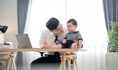 Fototapeta premium Father playing with baby at home workstation during daytime while working remotely in a modern and cozy environment