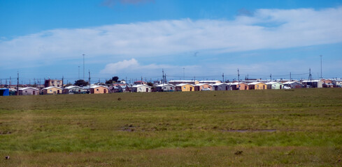 South Africa township settlement, rows of small, single-story houses, open grassy field, blue cloudy sky