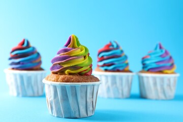 Delicious cupcakes with colorful cream on light blue background, selective focus