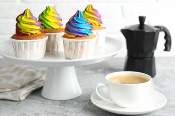 Delicious cupcakes with colorful cream and cup of coffee on grey textured table, closeup