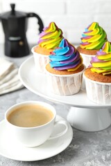 Delicious cupcakes with colorful cream and cup of coffee on grey textured table, closeup