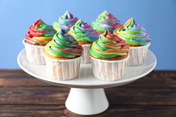 Delicious cupcakes with colorful cream on wooden table against blue background, closeup