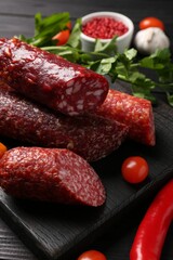 Different smoked sausages, tomatoes and chili pepper on black wooden table, closeup