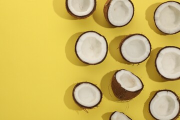 Halves of fresh coconuts on yellow background, flat lay. Space for text