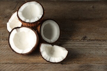 Pieces of cracked coconuts on wooden table, space for text