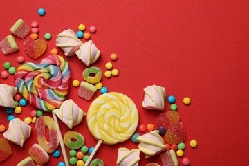 Many different tasty candies and marshmallows on red background, flat lay. Space for text