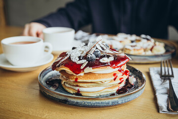 A tall stack of pancakes topped with coconut slices and blueberries.