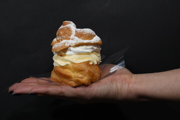 Elegant Hand Holding a Cream Puff Pastry with Whipped Cream and Vanilla Custard
