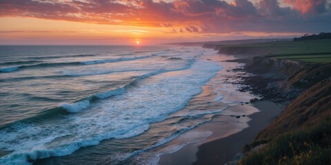 Sunset over ocean waves with rocky shoreline and grassy cliffs under colorful cloudy sky