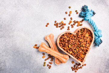 Heart-shaped bowl filled with dry dog ​​food. On gray concrete background. Top view.