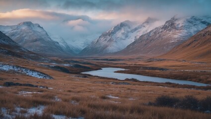 Fototapeta premium Mountain valley landscape with a river in the foreground under a cloudy sky and snow-capped peaks during dusk or dawn.