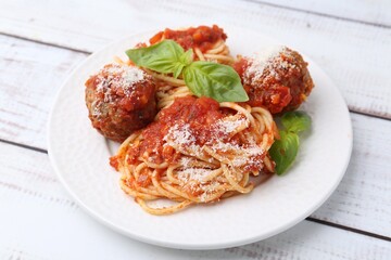 Delicious pasta with meatballs, cheese and basil on light wooden table, closeup
