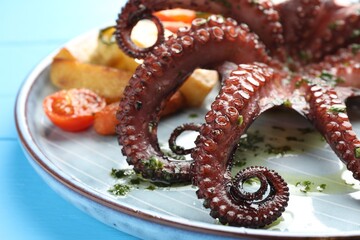 Fried octopus with herb sauce and vegetables on light blue wooden table, closeup
