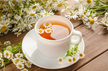 Chamomile tea in a white cup on a wooden background with a bouquet of daisies with selective focus