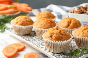 Tasty carrot muffins and fresh vegetables on white marble table, closeup