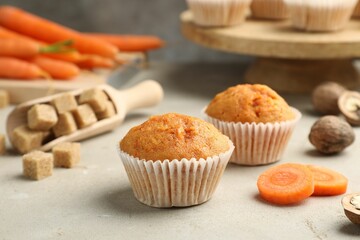 Tasty carrot muffins, fresh vegetables, sugar and walnuts on light grey table, closeup