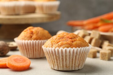 Tasty carrot muffins and cut vegetable on light grey table, closeup