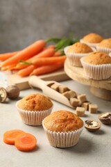 Tasty carrot muffins, fresh vegetables, sugar and walnuts on light grey table, closeup