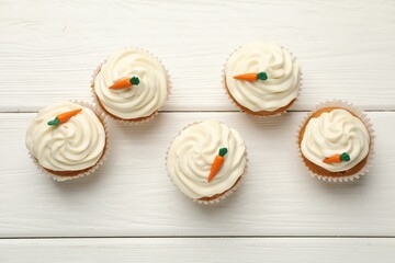 Tasty carrot muffins with cream on white wooden table, flat lay