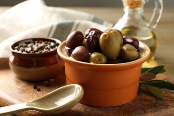 Tasty olives in bowl, leaves, oil and spices on wooden table, closeup