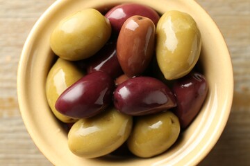 Tasty olives in bowl on wooden table, top view