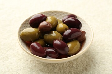 Tasty marinated olives in bowl on beige table, closeup