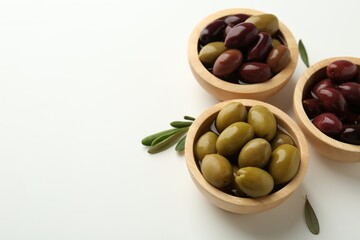 Tasty marinated olives in bowls and leaves on white table. Space for text