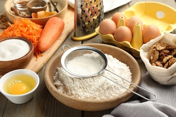 Different ingredients for making carrot cake and kitchenware on wooden table, closeup