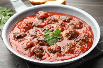 Delicious meatballs with tomato sauce in frying pan on wooden table, closeup