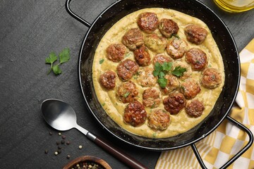 Delicious meatballs with gravy cream sauce and herbs served on black table, flat lay