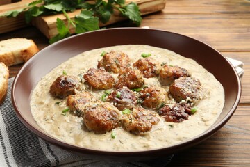 Delicious meatballs with gravy cream sauce and herbs served on wooden table, closeup